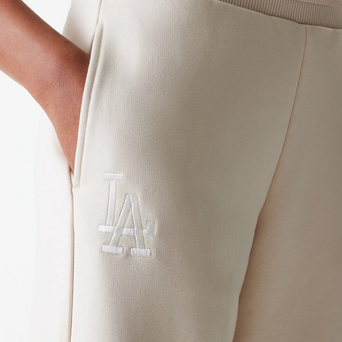 New Era LA Dodgers Womens MLB Tonal Light Beige Straight Leg Joggers, close-up showing the white embroidered LA logo on the upper leg, with a hand placed in the side pocket.