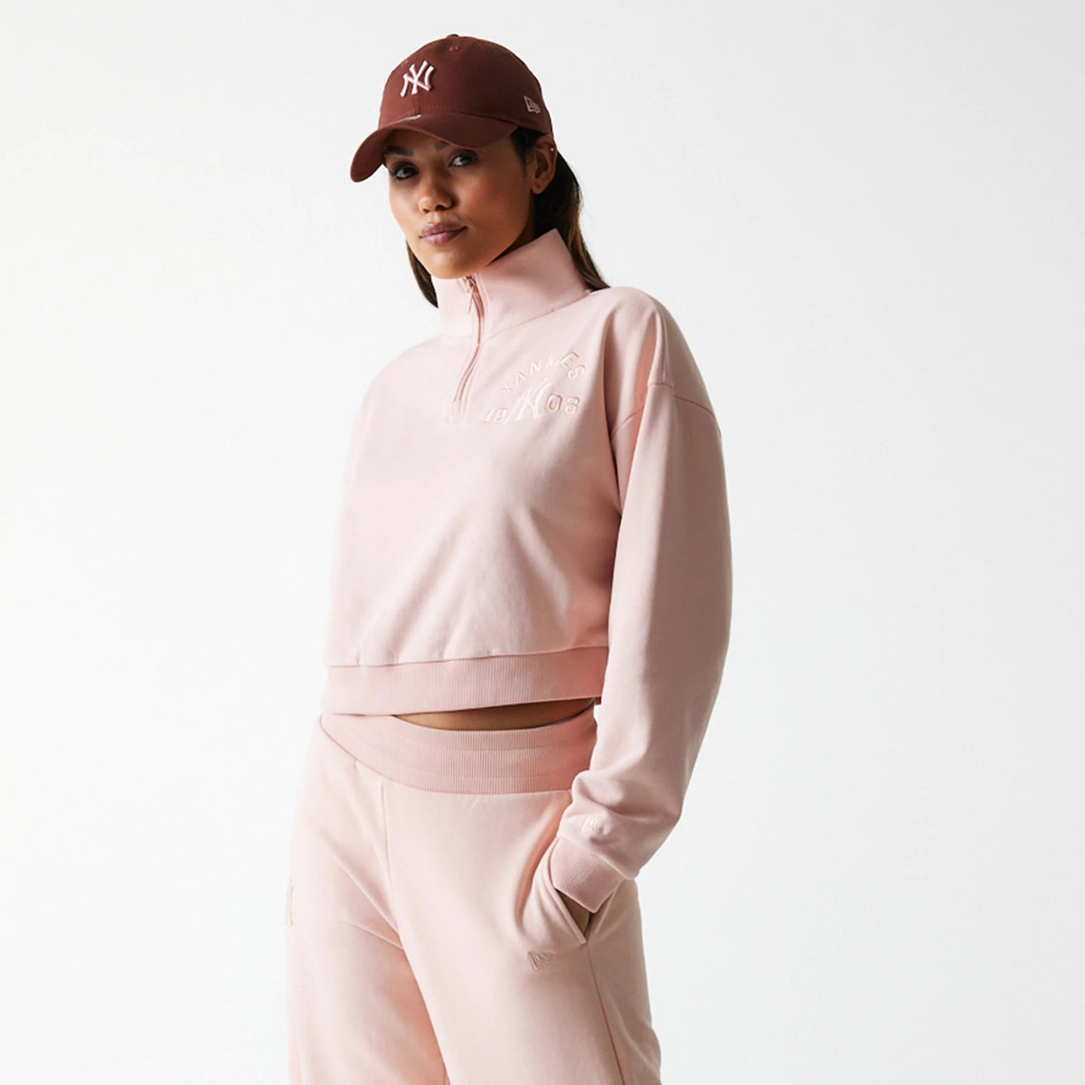 New Era New York Yankees Womens MLB Tonal Pastel Pink Cropped 1/4 Zip Sweater, front view on a model wearing matching pastel pink joggers, featuring a quarter zip at the high collar and tonal embroidered Yankees lettering on the chest.