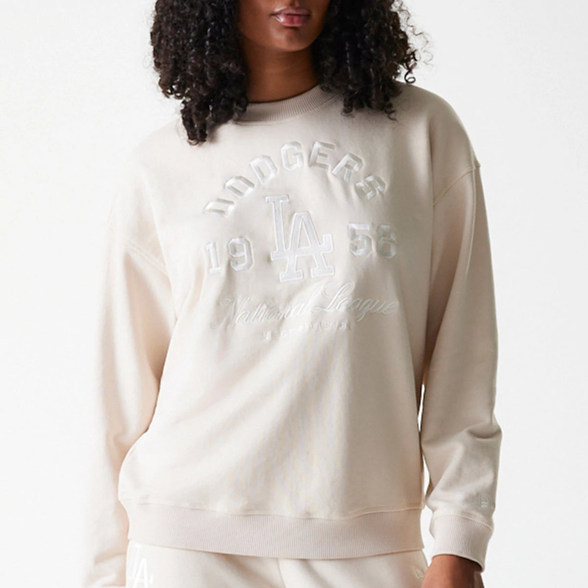 New Era LA Dodgers Womens MLB Tonal Graphic Light Beige Oversized Crew Neck Sweater, front view on a model with large raised embroidery featuring Dodgers 1958 and the LA logo across the chest, with ribbed cuffs and hem.