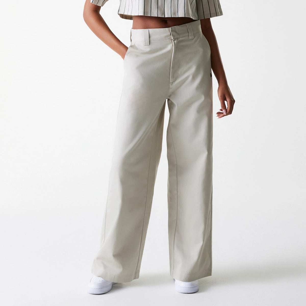 Womens New Era Light Beige Wide Leg Chino Trousers, front view on a model wearing a striped crop top, highlighting the high waist, belt loops, and relaxed fit of the wide legs draping over white trainers.