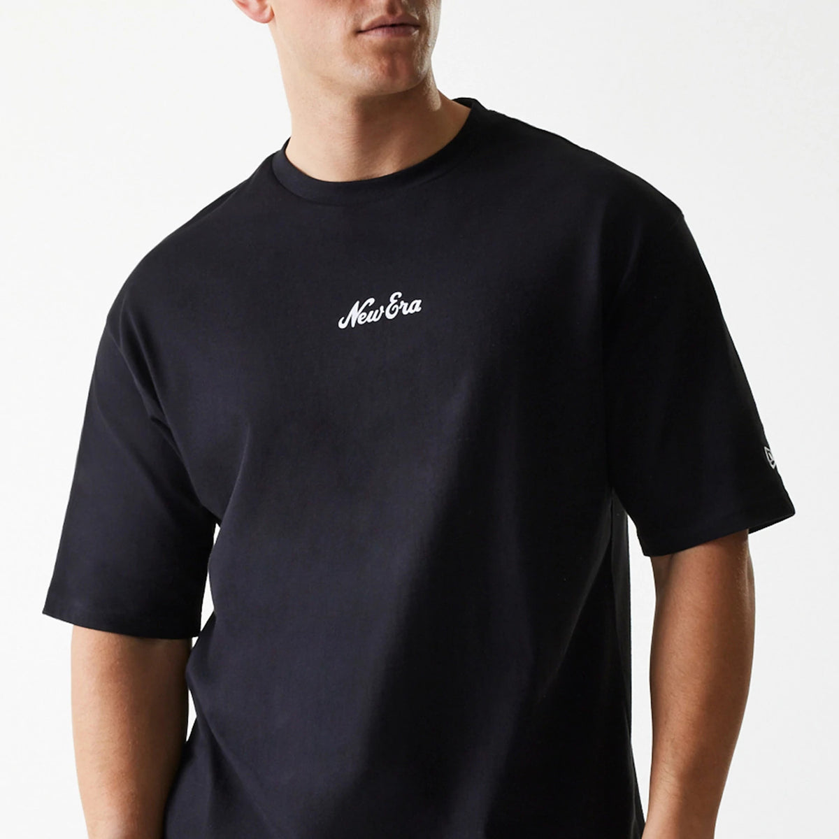 New Era Trucker Patch Black Oversized T-Shirt, on-model view showing the black T-shirt with the white embroidered New Era logo centred on the chest and a smaller logo on the short sleeve.