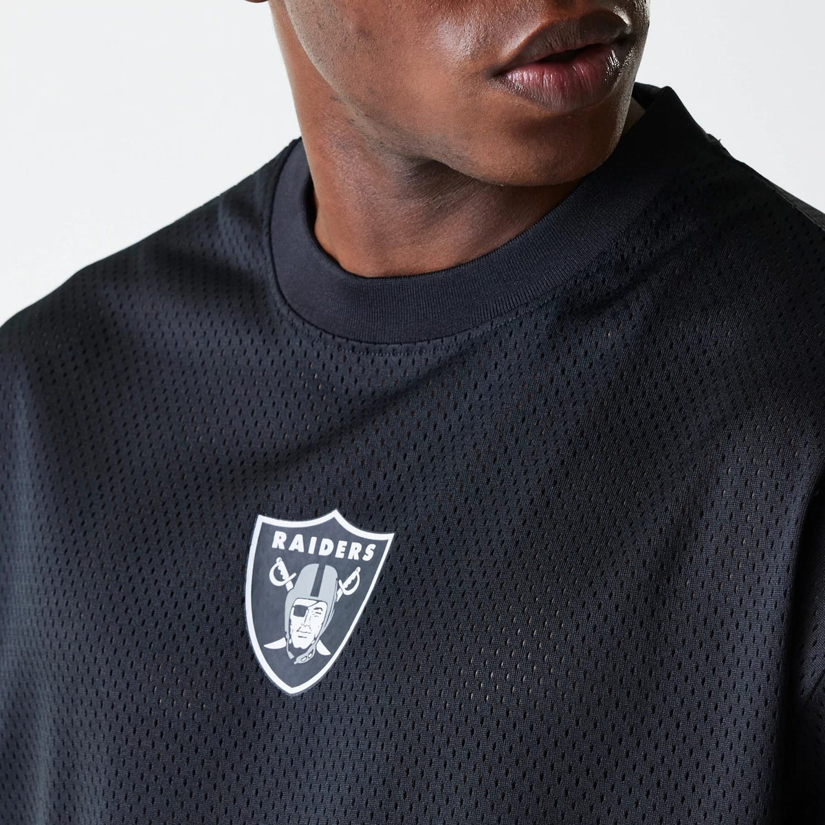 New Era Las Vegas Raiders NFL Essentials Black Oversized Mesh T-Shirt, front view showing the white embossed Raiders logo on the centre of the black mesh fabric, a rounded neckline and a glimpse of the shoulder seam.