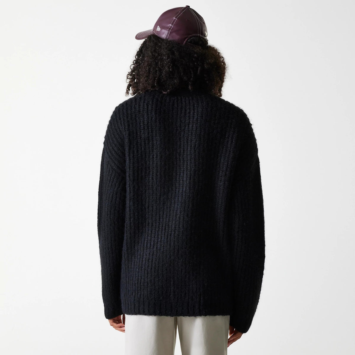 New Era New York Yankees Womens MLB Knit Black Cardigan, back view on a model wearing a burgundy cap, showing the cardigan's textured knit pattern and relaxed fit draping over white trousers.