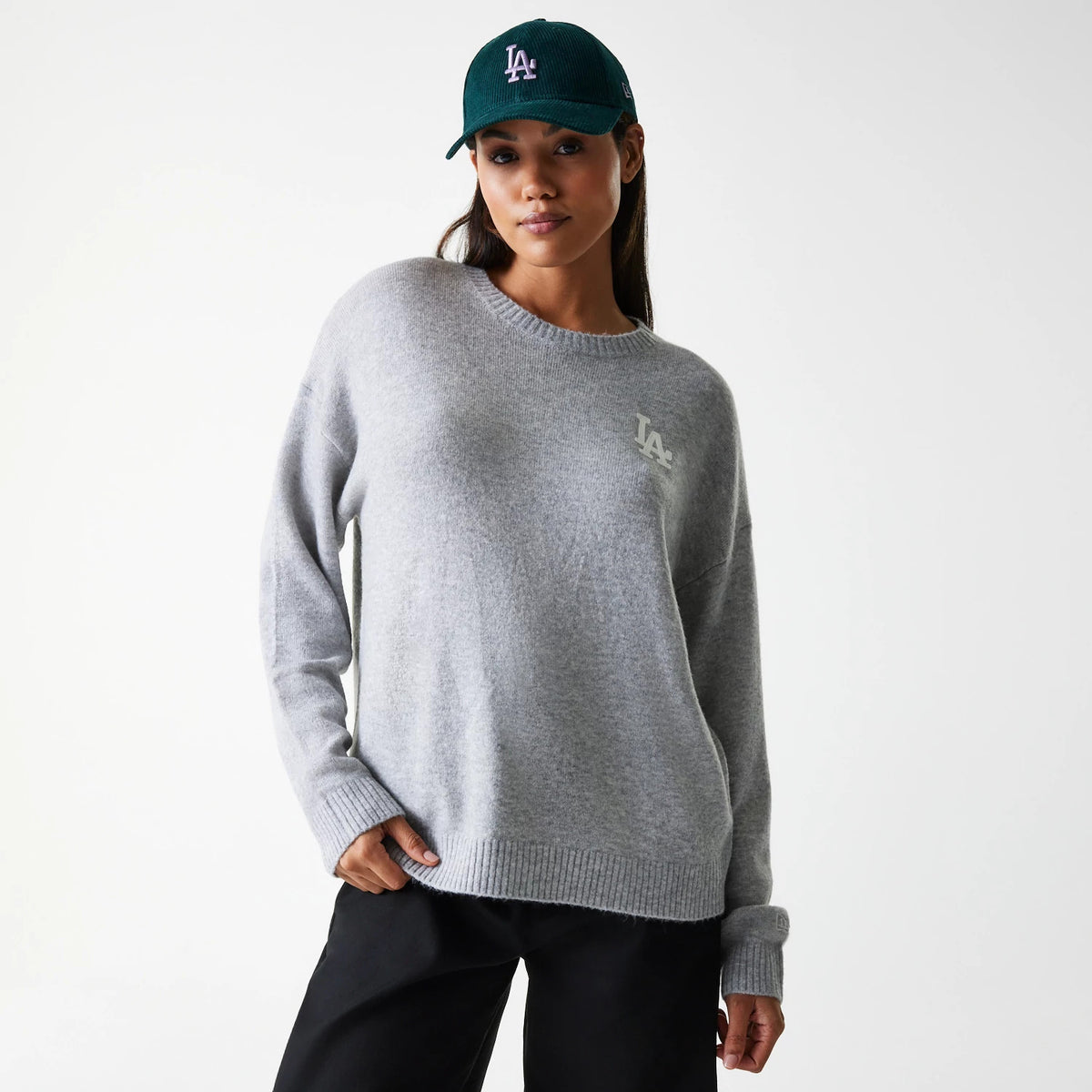 New Era LA Dodgers Womens MLB Knit Grey Crew Neck Sweater, front view on a model wearing a green cap, featuring the white LA logo embroidered on the left chest and a ribbed hem and cuffs.