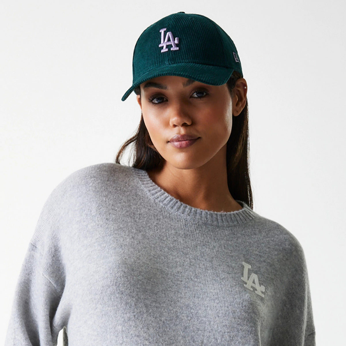 New Era LA Dodgers Womens MLB Knit Grey Crew Neck Sweater, on-model view showing a white embroidered LA logo on the left chest, paired with a green cap featuring a white raised LA logo on the front panel and an embroidered logo on the left side.