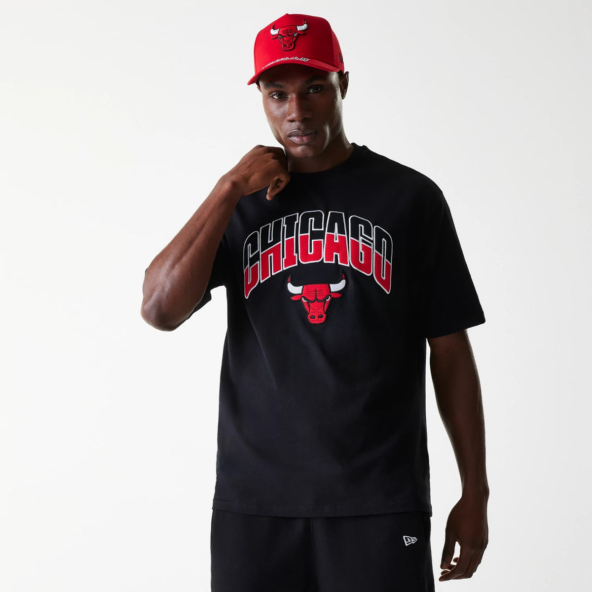 New Era Chicago Bulls NBA Arch Graphic Black Oversized T-Shirt, on-model view showing a red Chicago Bulls graphic prominently displayed on the chest, a raised red logo on a cap worn by the model, and a relaxed black fit.