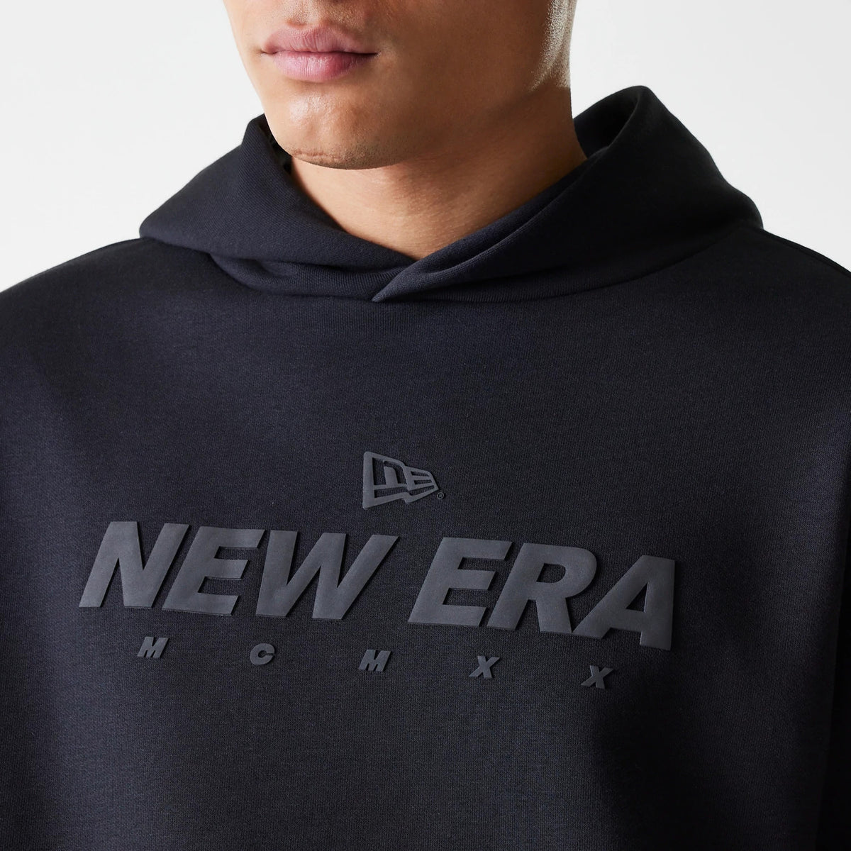 New Era Tech Black on Black Oversized Pullover Hoodie, front view showing the debossed New Era logo and large NEW ERA text across the chest, with a loose hood resting around the neck.