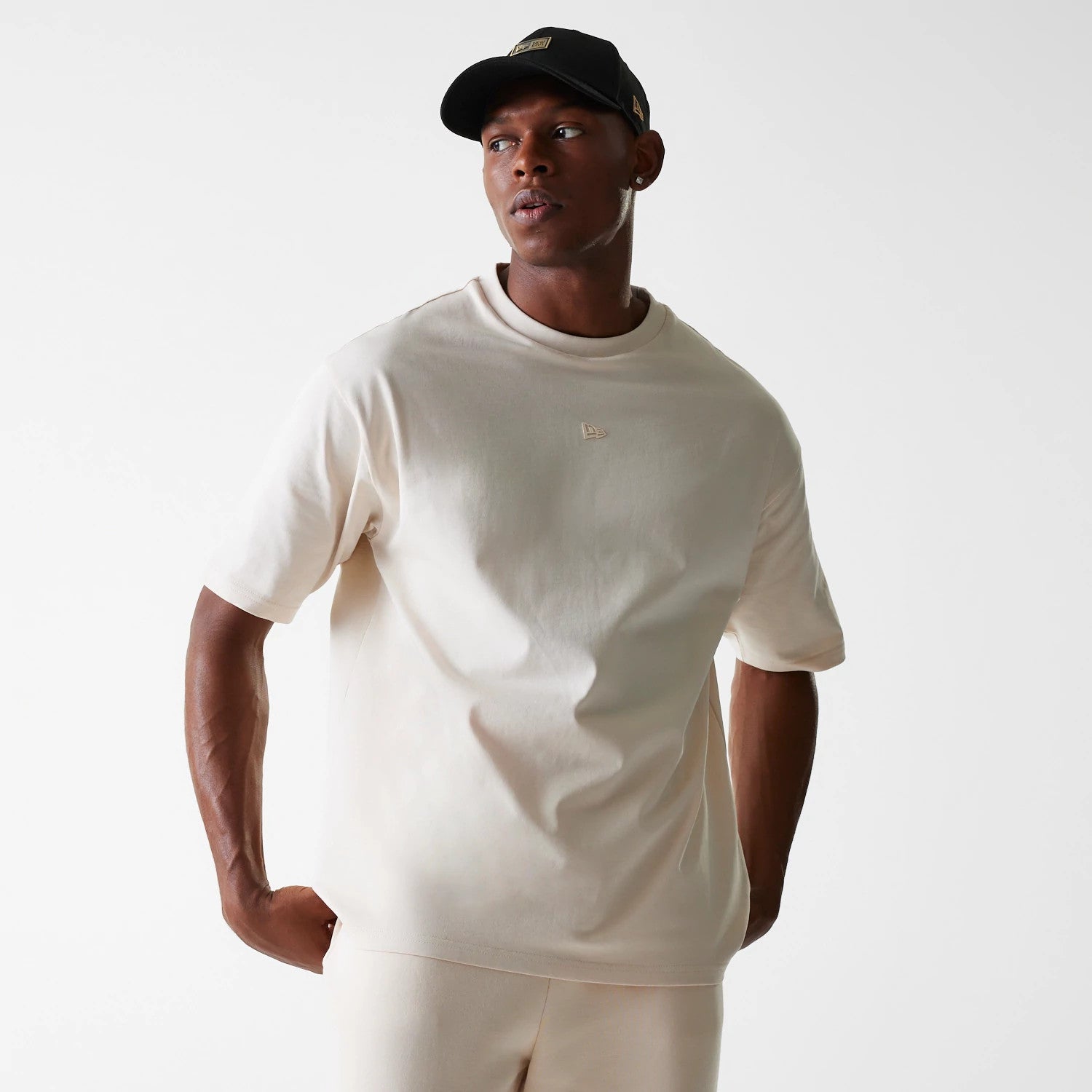 New Era Tech Light Beige Oversized T-Shirt, on-model view showing the light beige oversized fit with short sleeves, a small embossed New Era logo on the left chest, and plain design across the front.