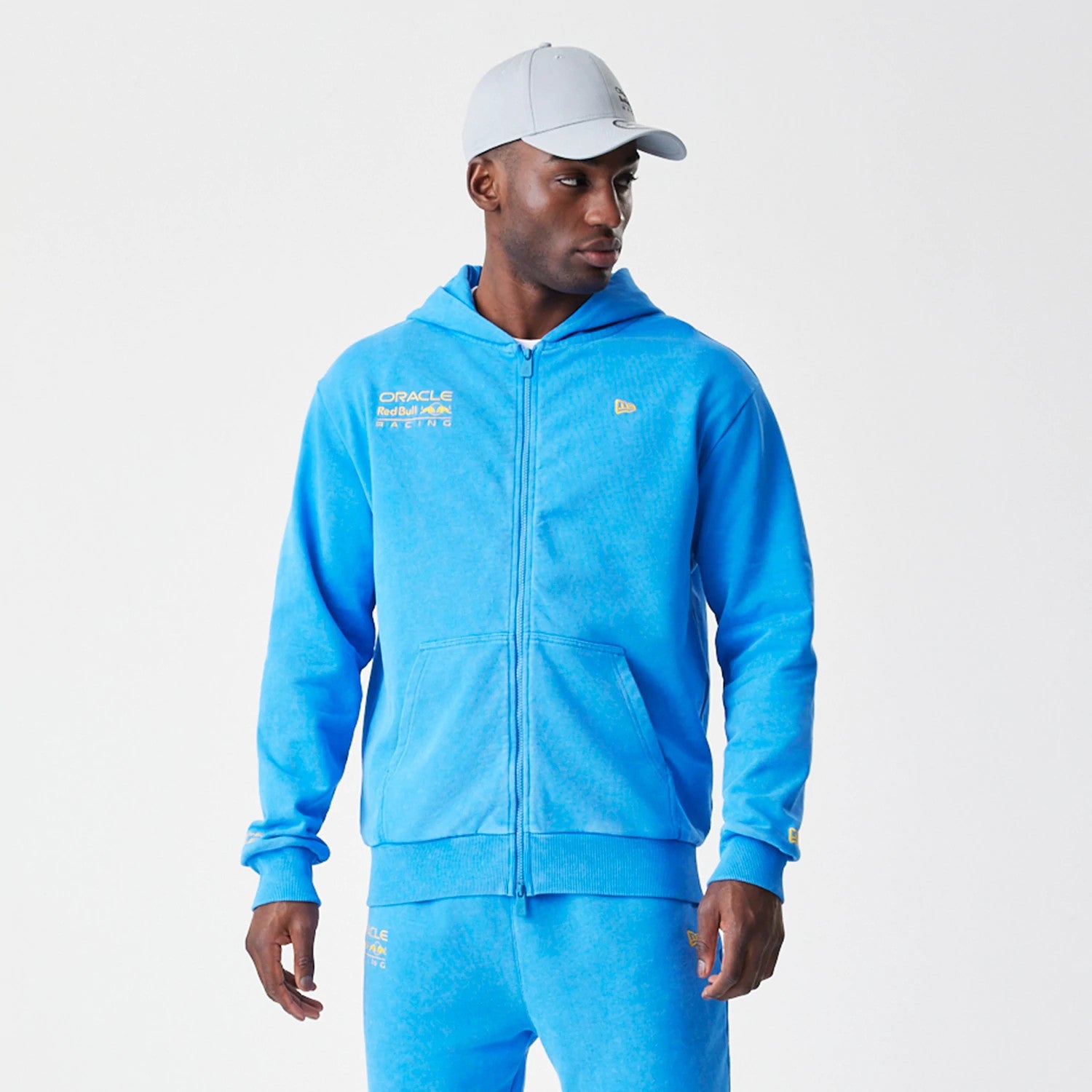 New Era Red Bull Racing Blue Oversized Full Zip Hoodie, front view on a model styled with matching trousers and a cap, featuring a gold embroidered New Era logo on the chest and sleeve with Red Bull Racing text across the upper chest.