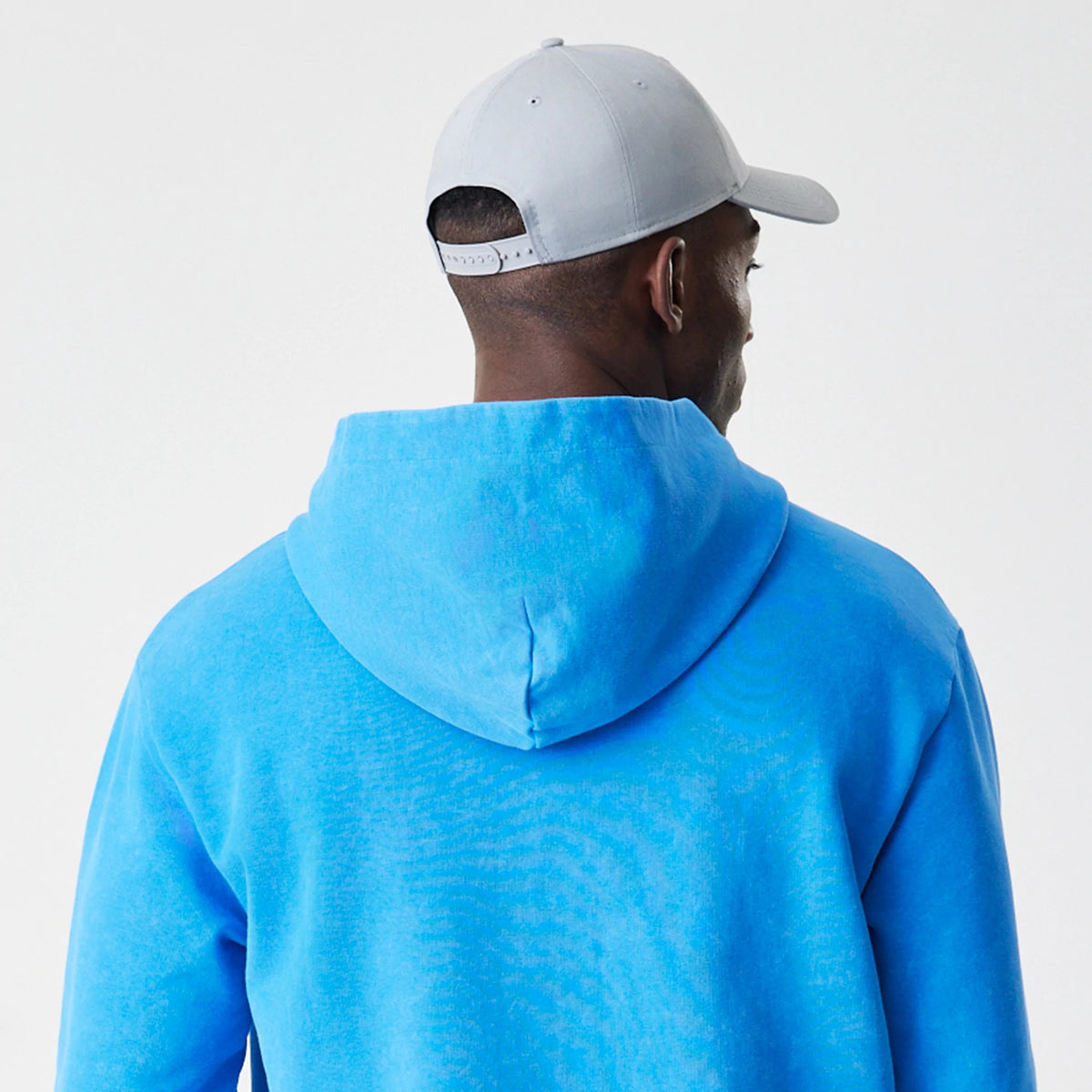 New Era Red Bull Racing Blue Oversized Full Zip Hoodie, back view on-model showing the blue hood draped naturally, paired with a light grey cap, creating a casual and sporty styling.
