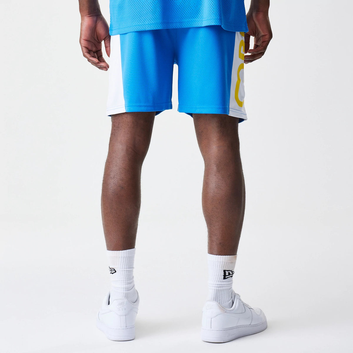 New Era Red Bull Racing Graphic Mesh Blue Shorts, back view on a model showcasing blue mesh fabric with contrasting white side panels and a large yellow printed graphic running vertically down the right leg.