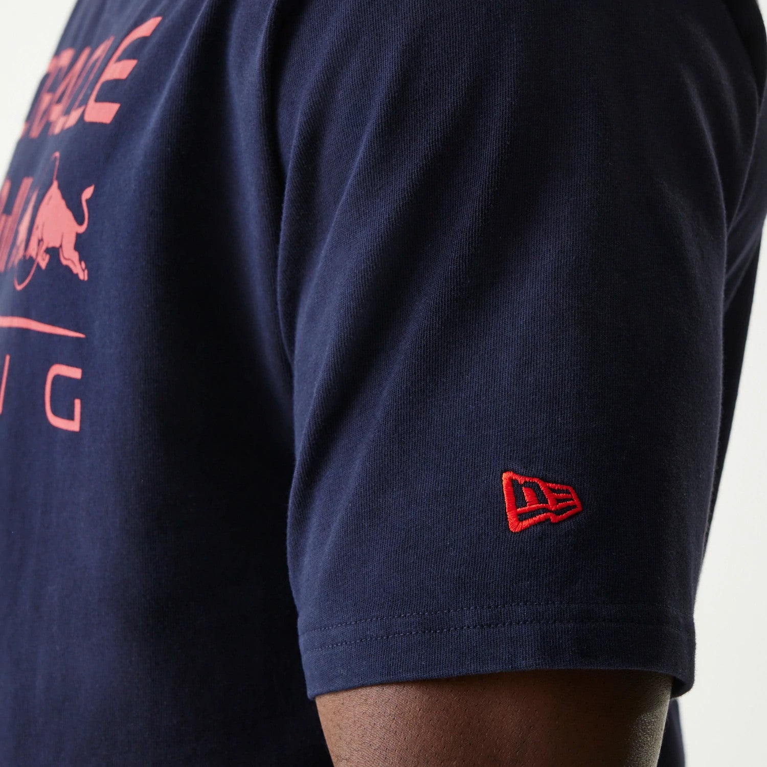 New Era Red Bull Racing Dark Blue Oversized T-Shirt, side view showing the short sleeve with a red embroidered New Era logo near the hem and a view of the pink Red Bull Racing graphic across the chest.