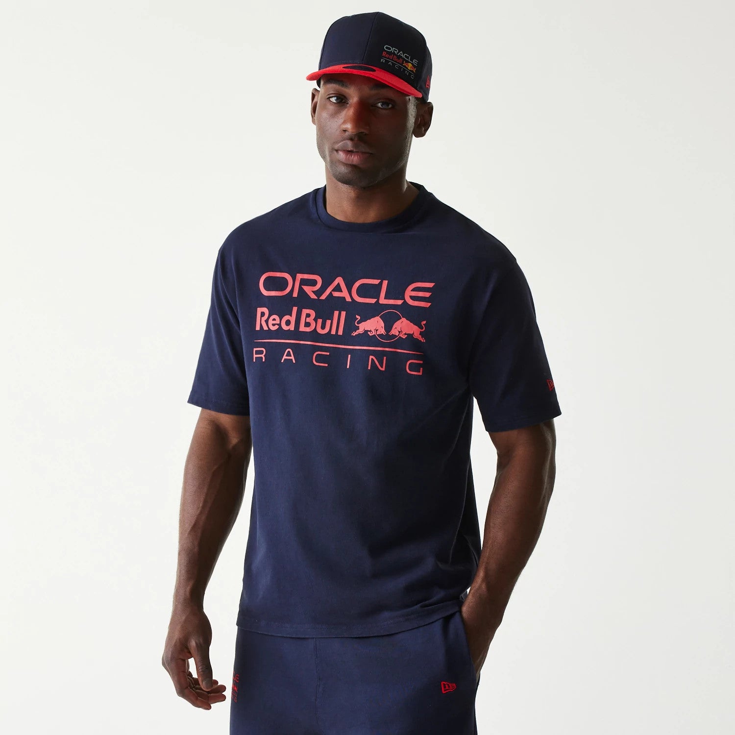 New Era Red Bull Racing Dark Blue Oversized T-Shirt, front view on-model with a matching cap, featuring red printed Oracle Red Bull Racing lettering and logo across the chest and a small red New Era logo on the left sleeve.