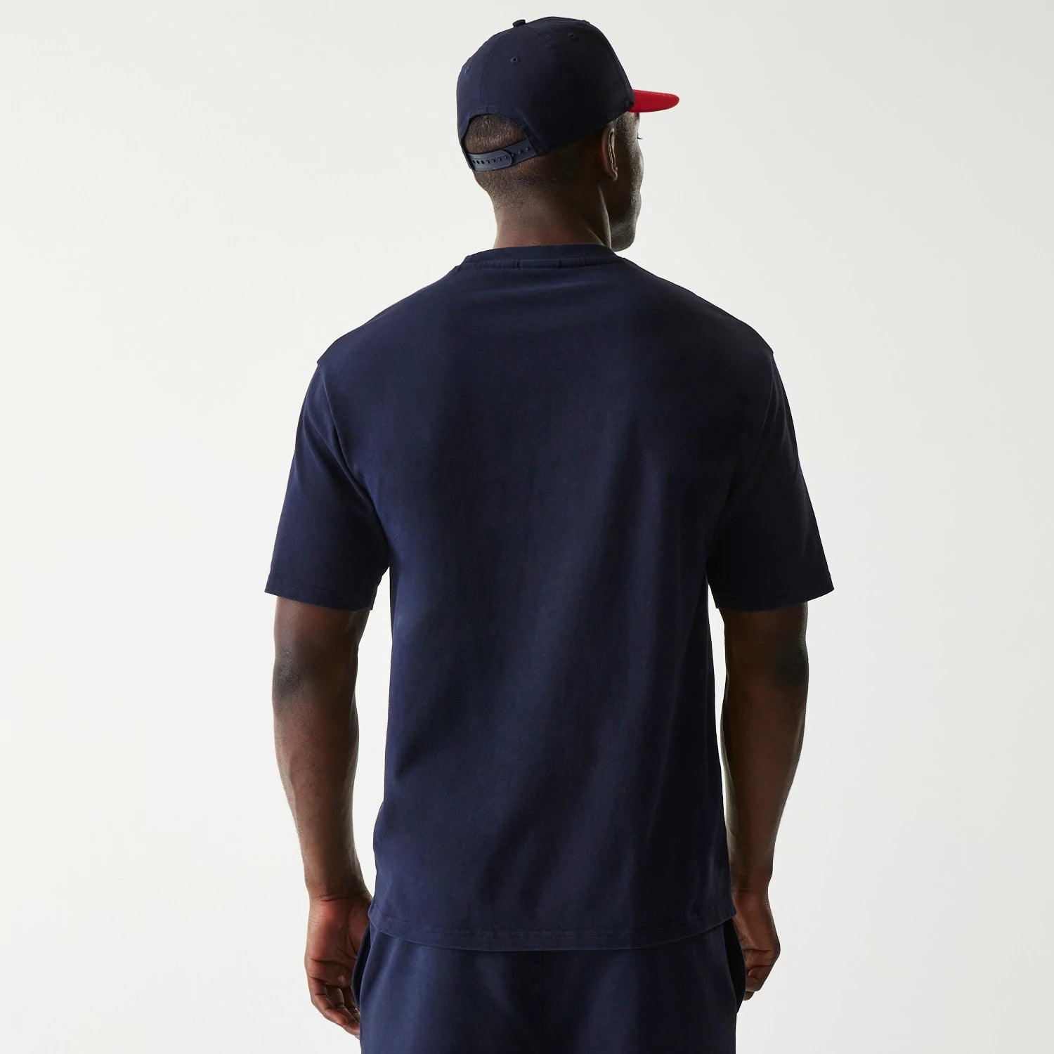 New Era Red Bull Racing Dark Blue Oversized T-Shirt, back view on-model showing the plain dark blue canvas with no additional graphics, complemented by a matching cap with a contrasting red visor.