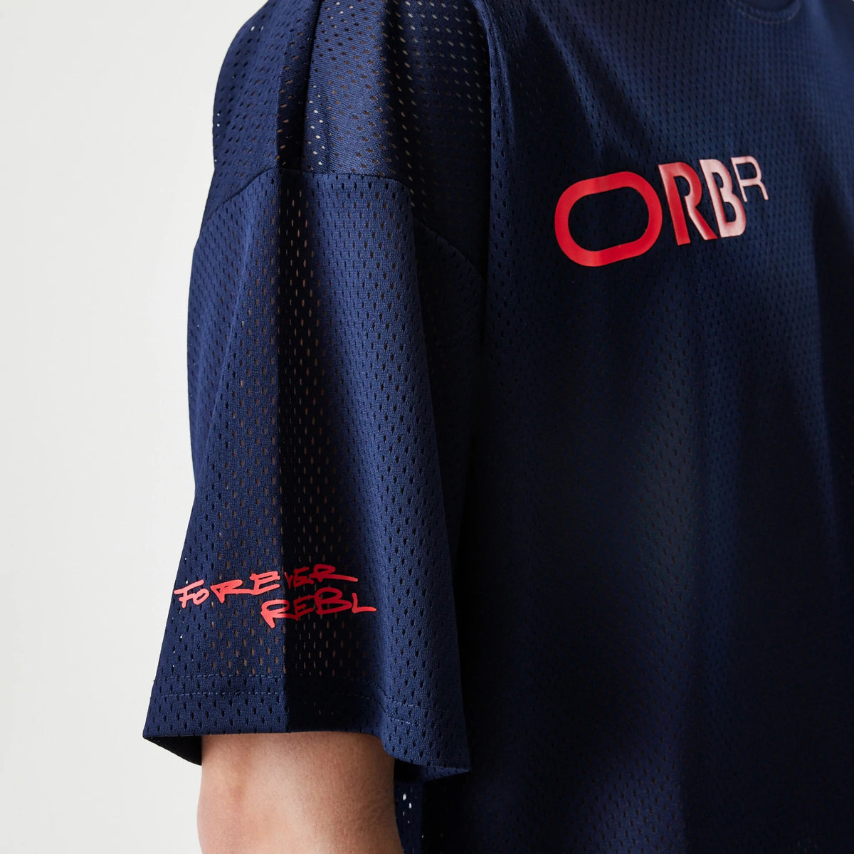 New Era Red Bull Racing Graphic Mesh Dark Blue Oversized T-Shirt, side view showing the mesh design, red embossed ORBR logo on the chest, and a Forever Rebl graphic printed in red on the sleeve.