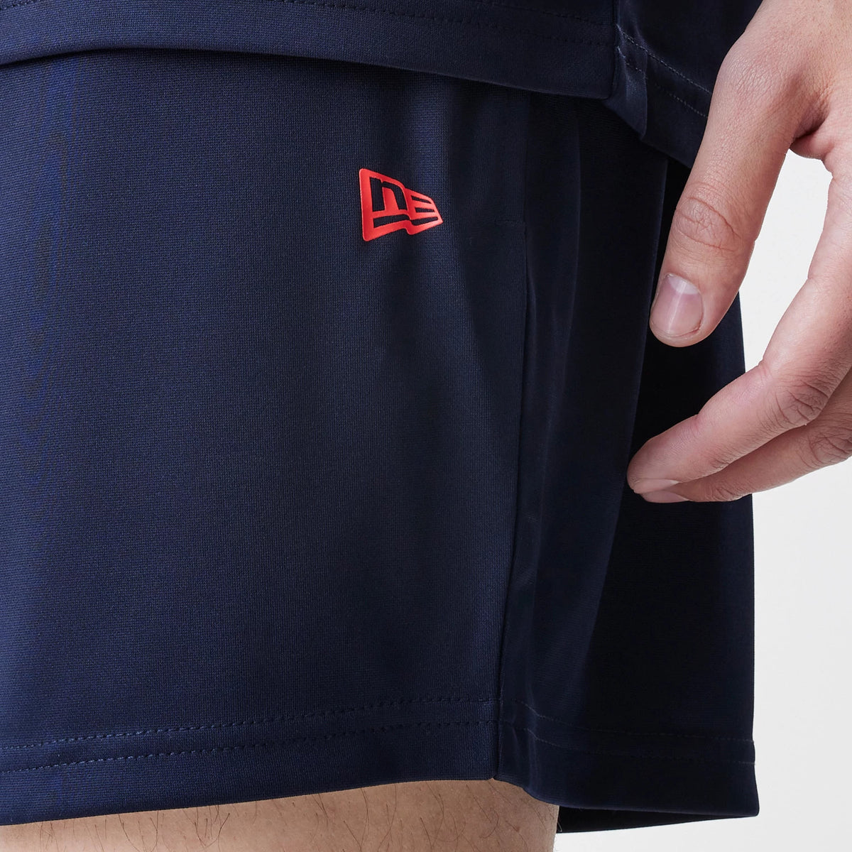 New Era Red Bull Racing Graphic Dark Blue Football Shorts, side view showing a close-up of dark blue fabric with a red embroidered New Era logo positioned on the left side, demonstrating the minimalist design of the shorts.