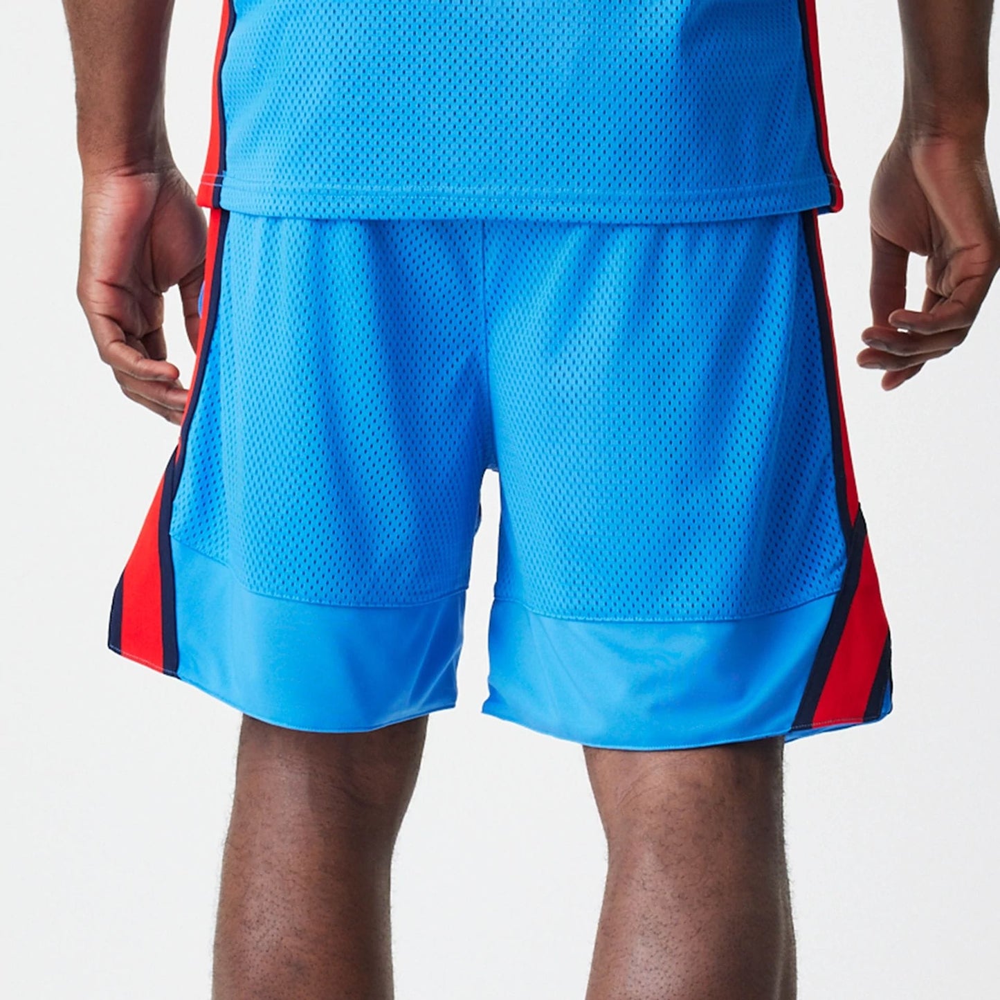 New Era Red Bull Racing Basketball Mesh Blue Shorts, back view on a model showing the blue mesh fabric, elastic waistband, and contrasting red and black side stripes extending down the legs.
