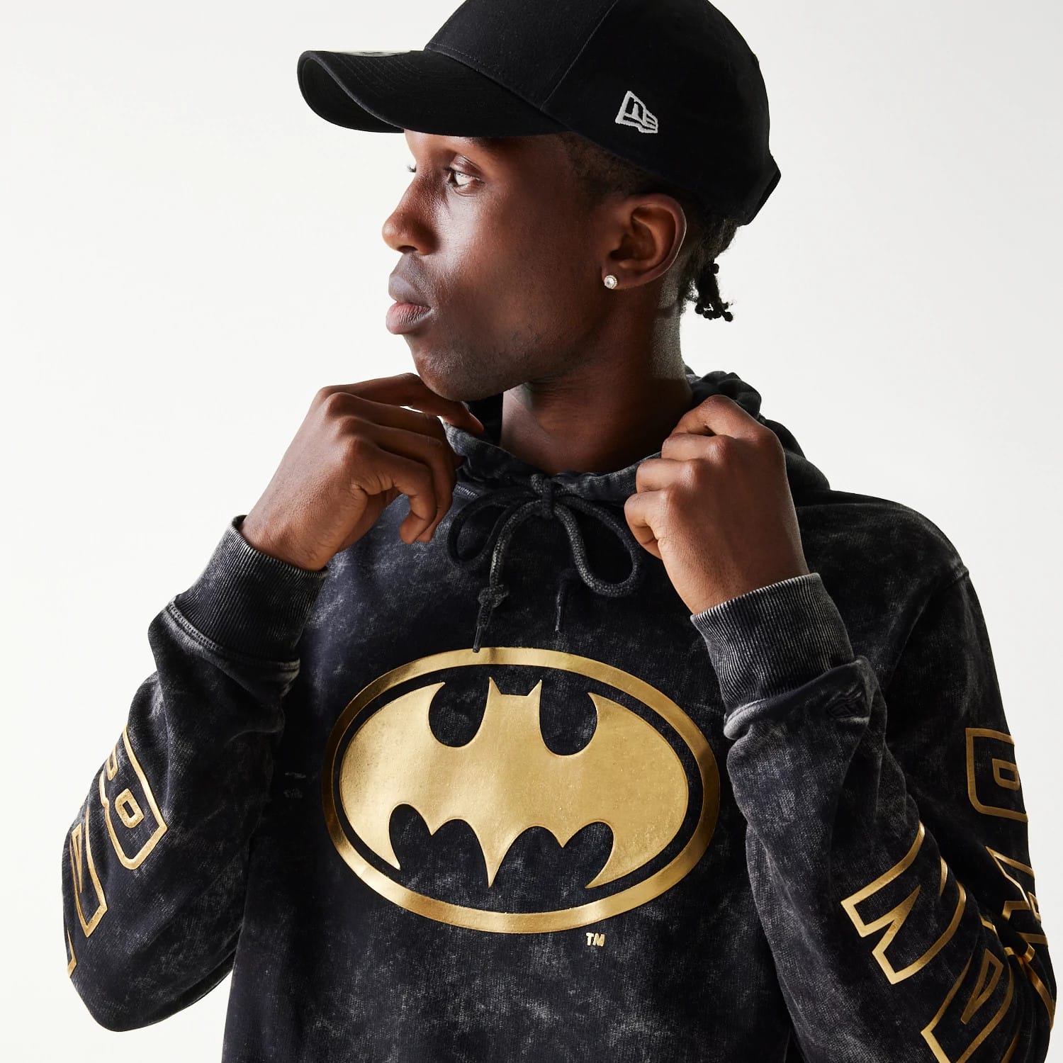 New Era Batman 1989 Black Pullover Hoodie, front view on-model showing a large gold Batman logo centred on the chest, gold lettering along the sleeve, and a drawstring hood worn visibly around the neck.