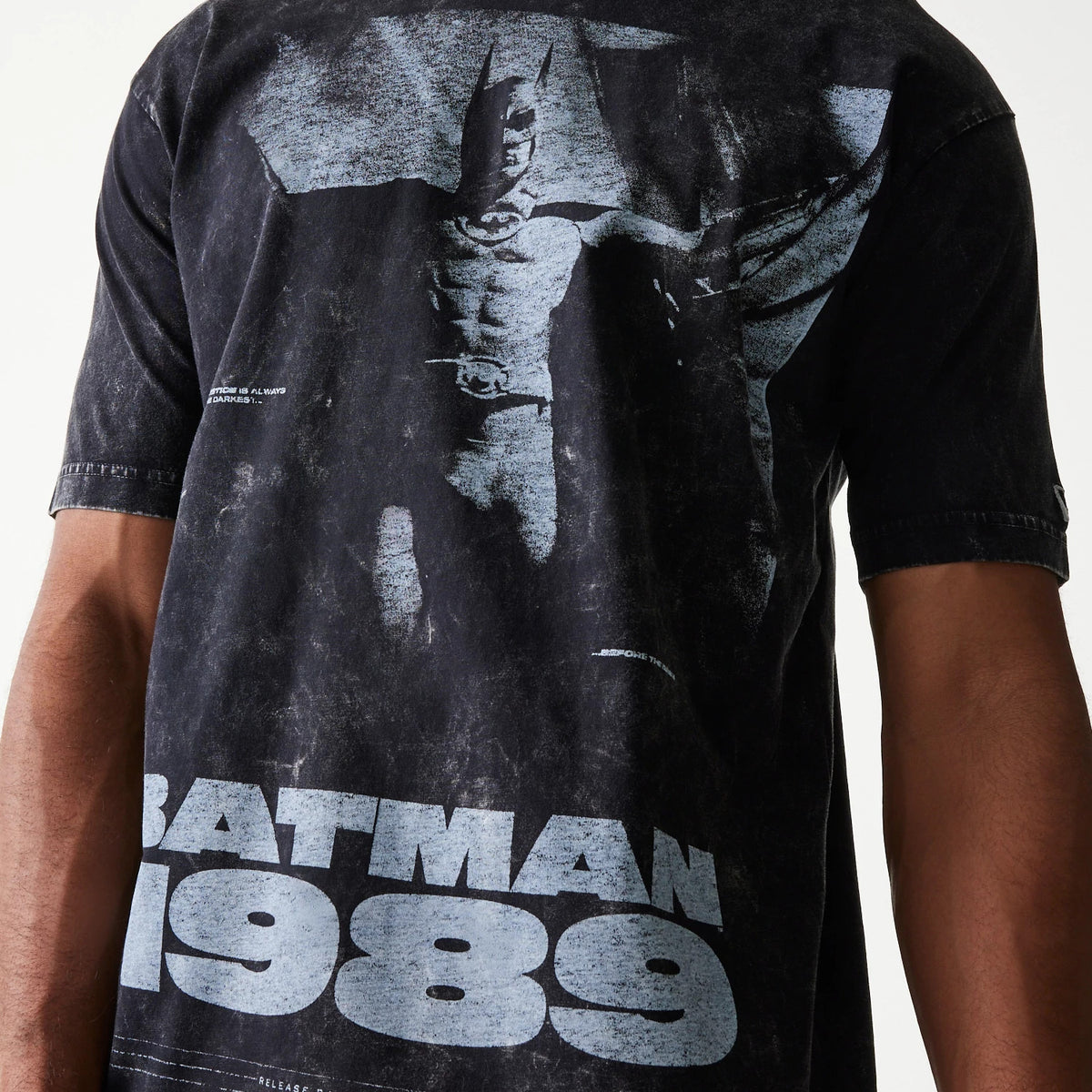 New Era Batman 1989 Black T-Shirt, front view showing a faded graphic of Batman in grey with large Batman 1989 text beneath, worn by a model and featuring a New Era logo on the left sleeve.