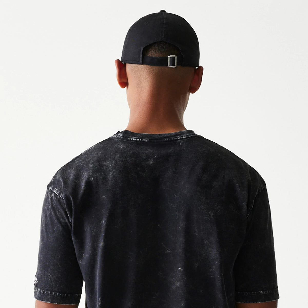 New Era Batman 1989 Black T-Shirt, back view on a model showing the distressed black fabric surface, a simple crew neck design, and a small embroidered New Era logo on the sleeve edge.