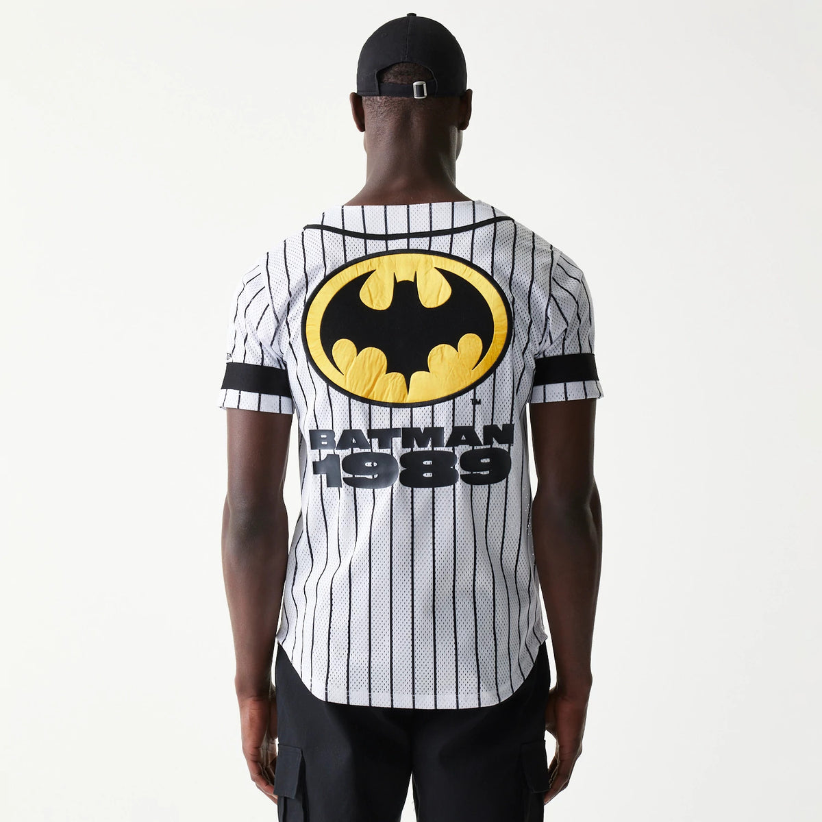 New Era Batman Pinstripe White Jersey, back view on a model showing the large yellow and black Batman logo and Batman 1989 lettering on a white mesh background with vertical black pinstripes.