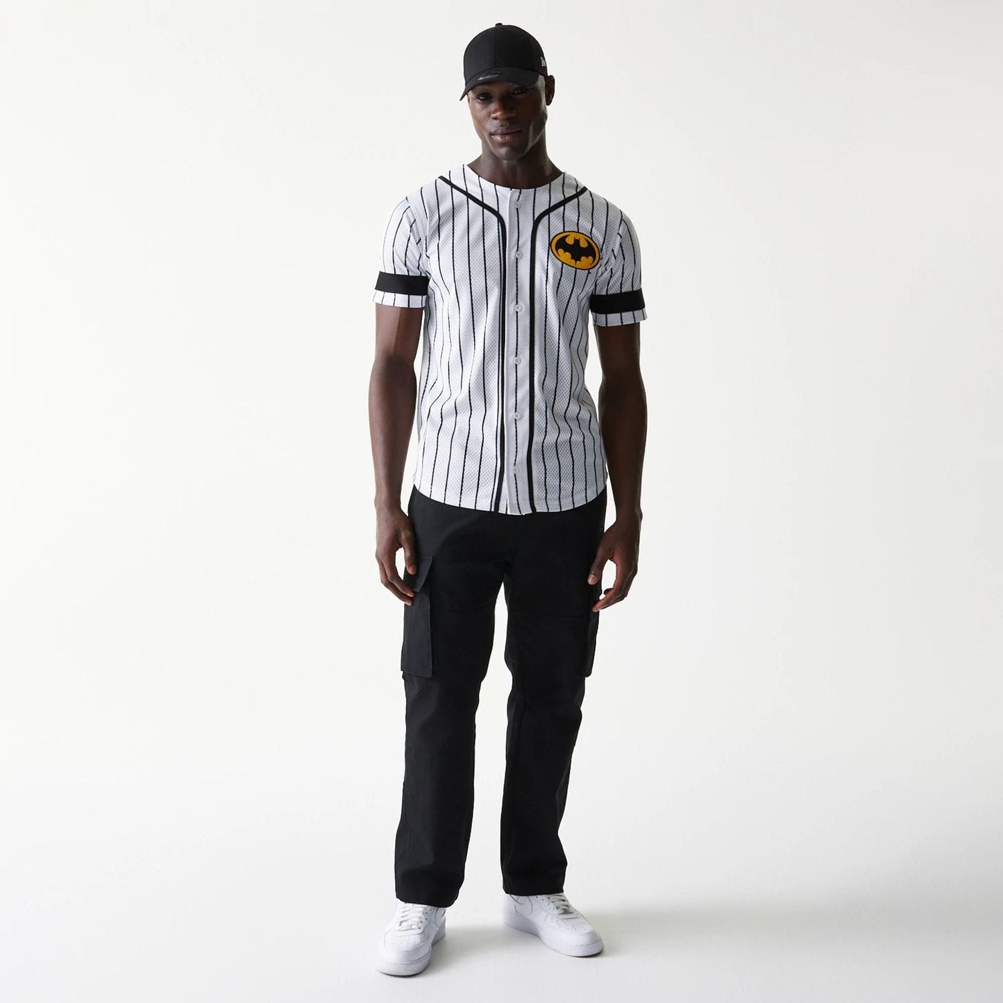 New Era Batman Pinstripe White Jersey, front view on a model with the yellow and black Batman logo on the left chest, featuring vertical black pinstripes, black shoulder piping, and sleeve cuffs.