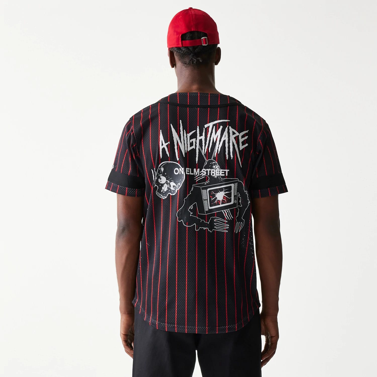 New Era A Nightmare On Elm Street Black Jersey, back view on a model wearing a red cap, with white horror-themed graphics including skull and TV motifs against a black background with red vertical stripes.
