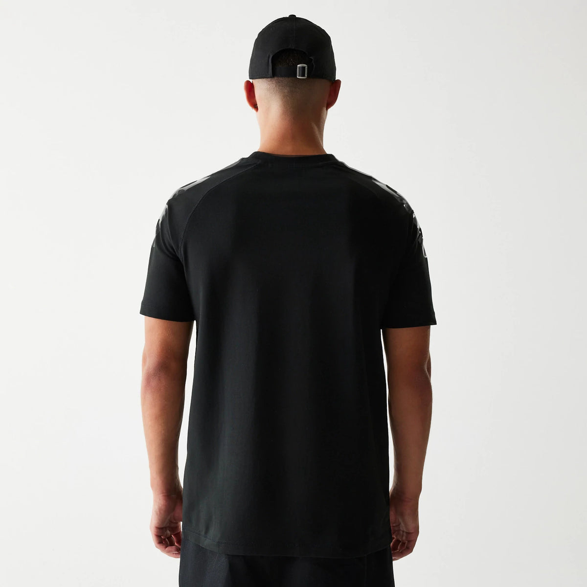 New Era Green Bay Packers NFL 3RD Down Black T-Shirt, back view on-model showing the plain black back with short sleeves and black panels over each shoulder, styled with a matching black cap worn backwards.
