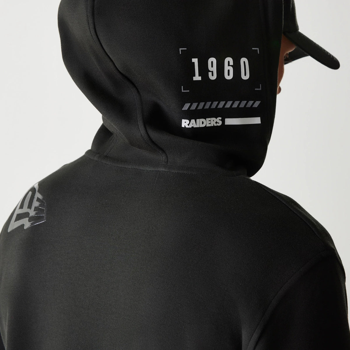 New Era Las Vegas Raiders NFL 3RD Down Black Pullover Hoodie, back view showing 1960 and Raiders lettering in white on the hood, and a raised Raiders logo on the shoulder, styled on a person with a matching black cap.
