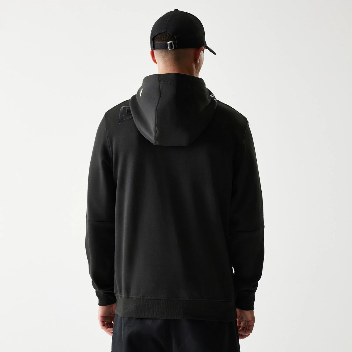 New Era Las Vegas Raiders NFL 3RD Down Black Pullover Hoodie, back view showing a plain black design with the hood down and details at the shoulders, worn by a model with a matching black cap.