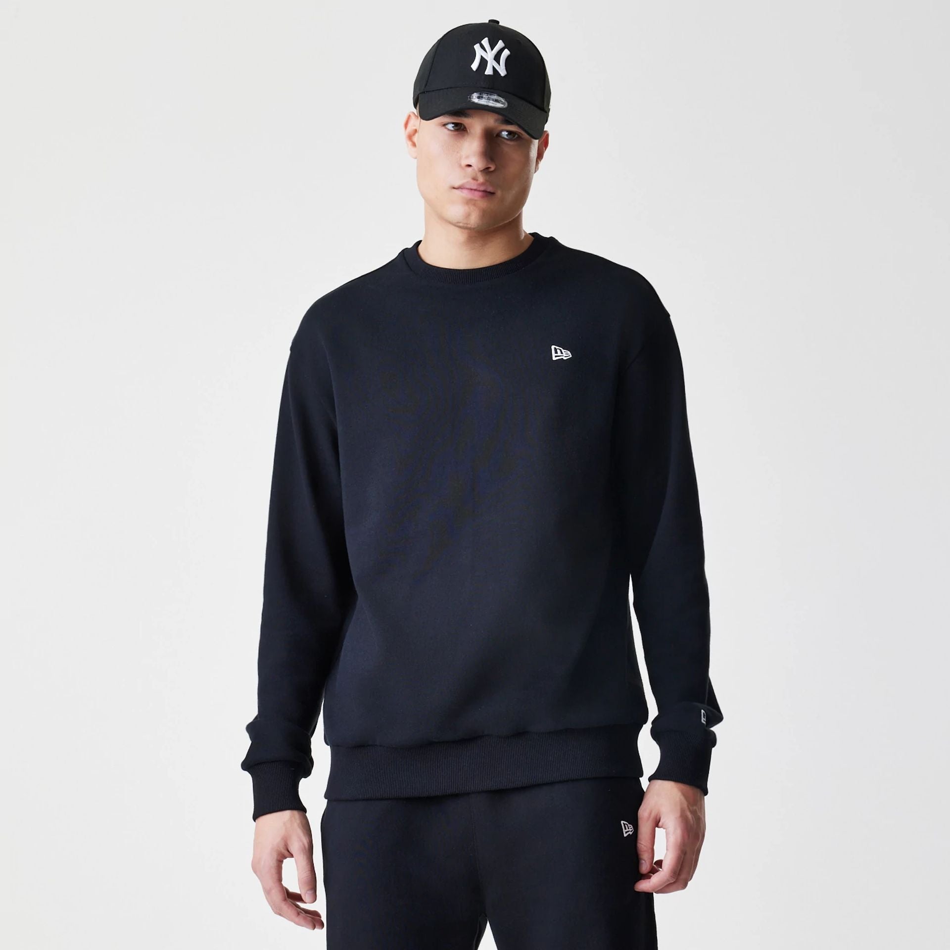 The Male model is wearing New Era Premium Essential Black Oversized Crew Neck Sweater 1