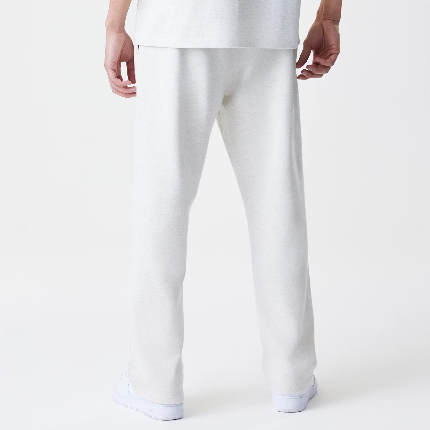 New Era Premium Essential Pastel Grey Joggers, rear view on a model showing the relaxed fit and straight leg design, with a texture in the pastel grey fabric and white trainers completing the look.