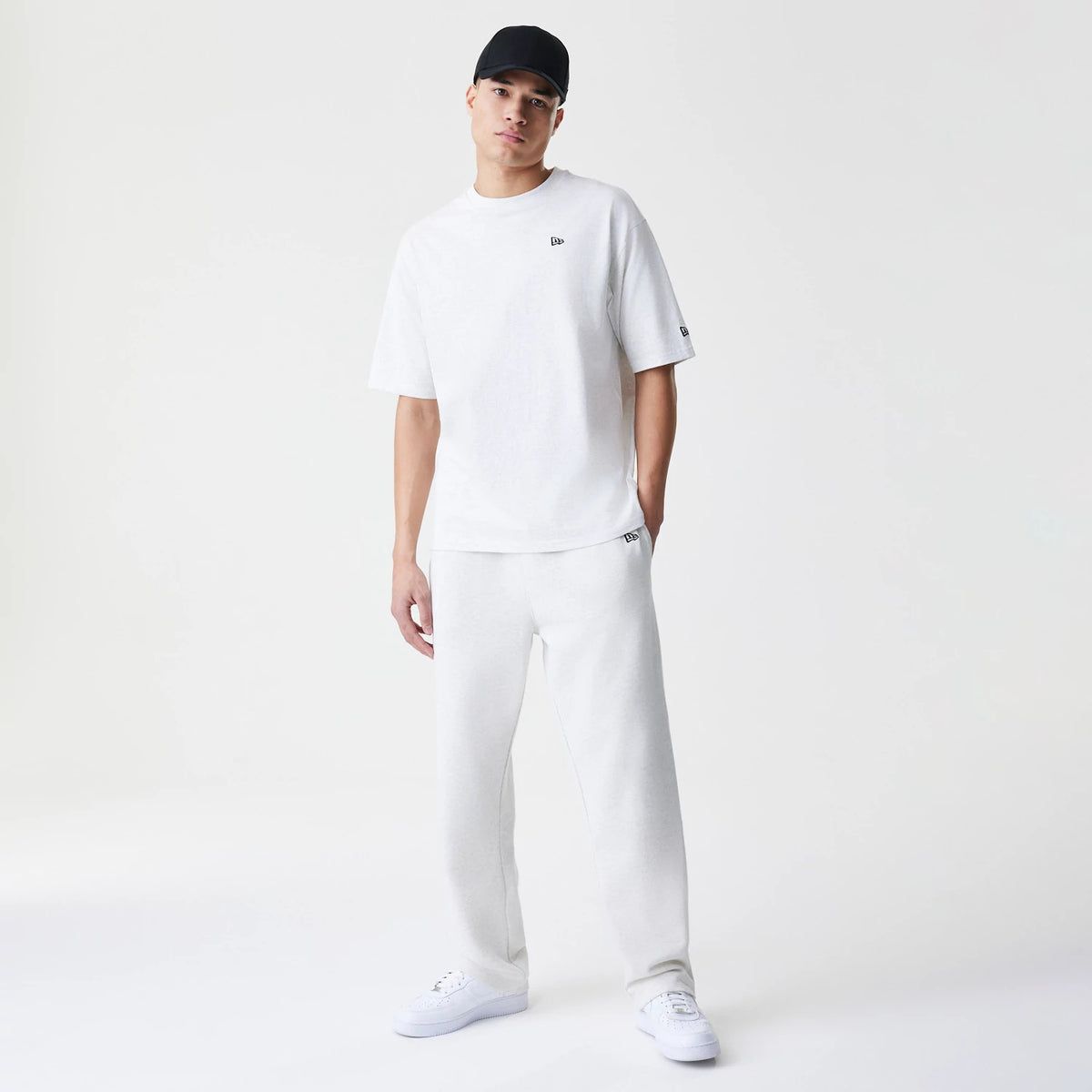 New Era Premium Essential Pastel Grey Joggers, on-model view showing relaxed fit and elasticated waistband, paired with a plain white T-shirt featuring a small black New Era logo on the chest.