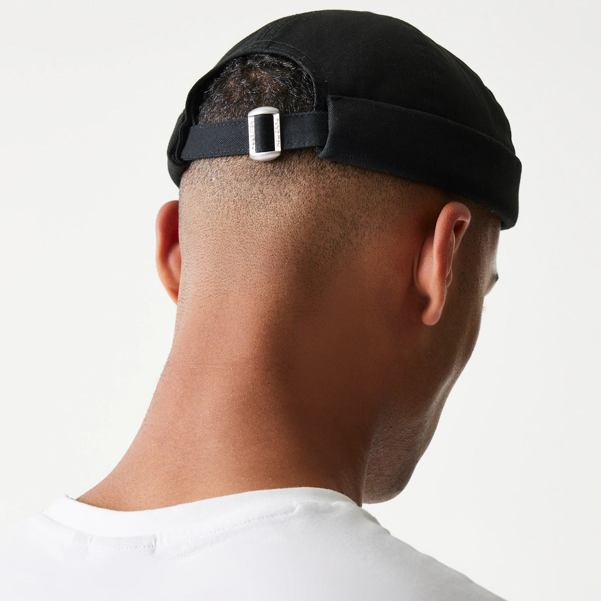 New Era Cotton Twill Black Docker Hat, rear view on a model showing the adjustable strap with a silver buckle at the back, highlighting the snug fit and simple design of the black cotton twill fabric.