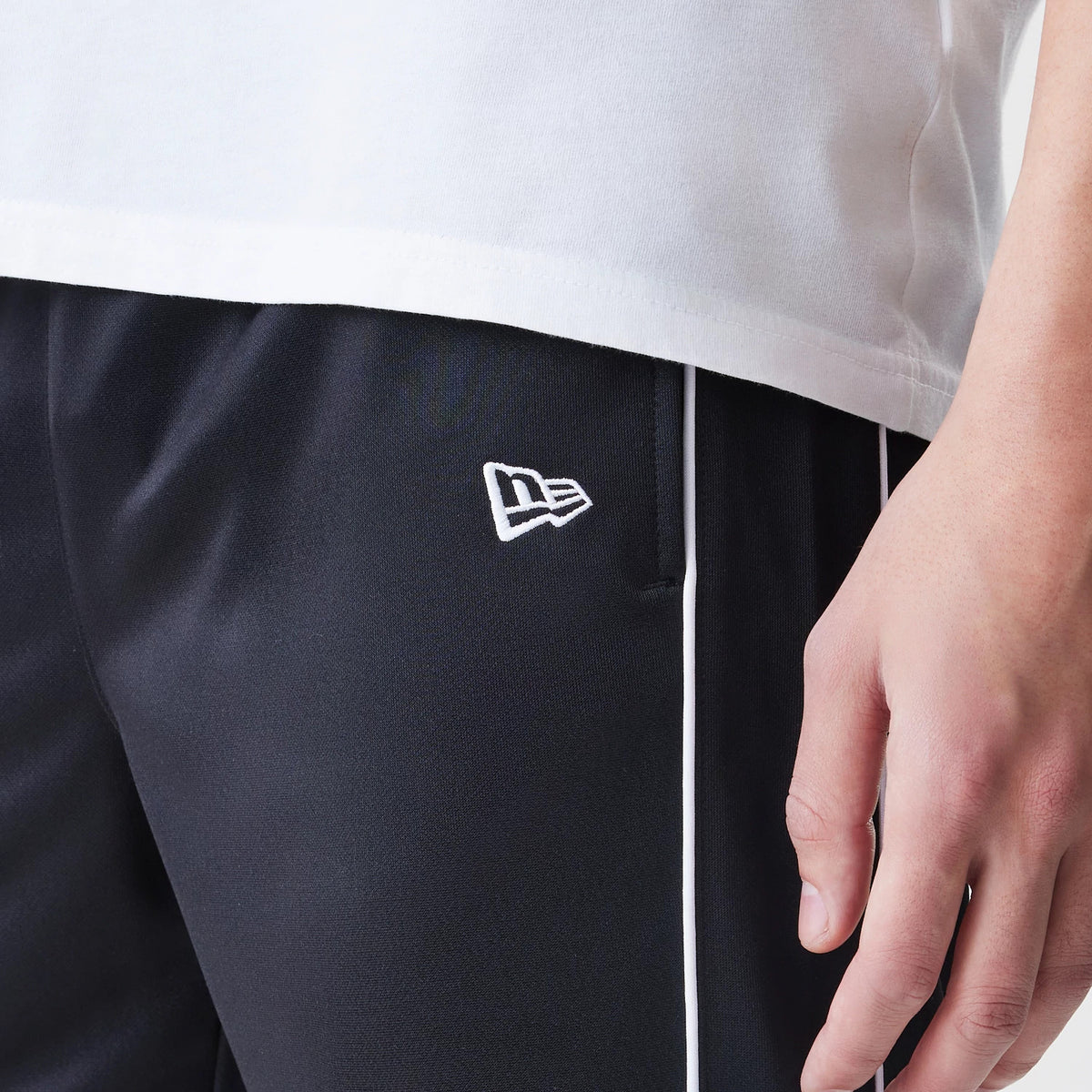 New Era Chicago Bulls NBA Slim Black Track Pants, close-up on a model showing the New Era flag logo embroidered in white near the pocket with contrasting white piping along the side seam and a black fabric.