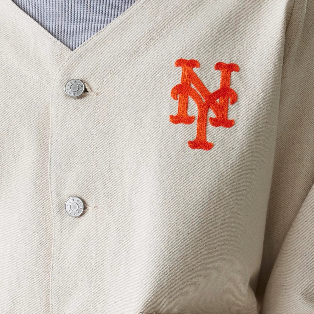 New Era New York Mets MLB Cotton Open Cream Jacket, front view showing an orange embroidered Mets logo on the left chest, two button fastenings down the front, and a V-shaped neckline.