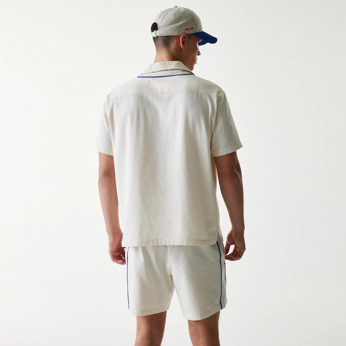 New Era New York Mets MLB Piping Open Cream Short Sleeve Shirt, back view on a model wearing matching cream shorts, featuring blue piping along the collar and shoulders for a classic baseball-inspired look.