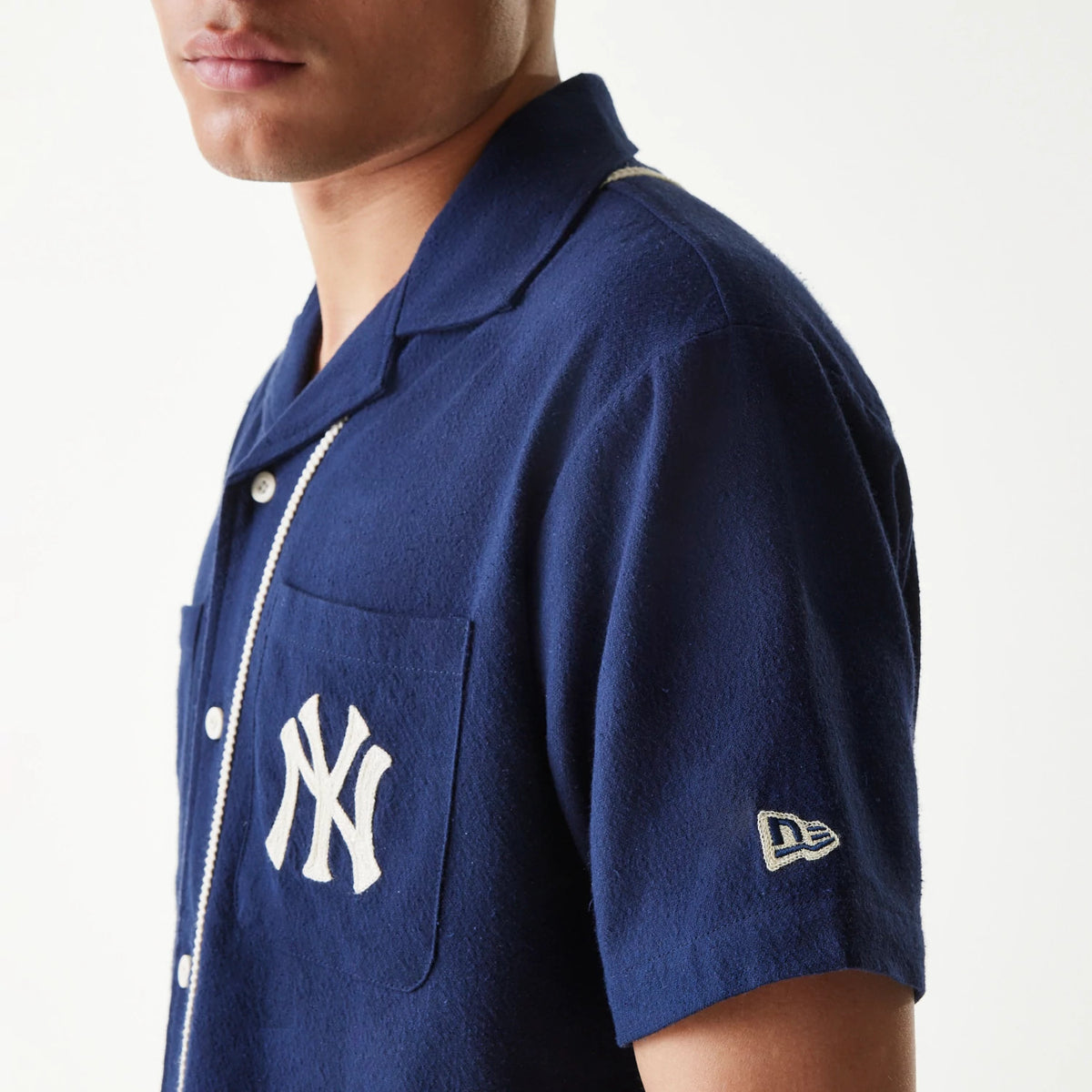 New Era New York Yankees MLB Piping Navy Short Sleeve Shirt, side view on a model showing the white embroidered NY logo on the chest pocket, button-down front with white piping, and New Era flag logo on the sleeve.