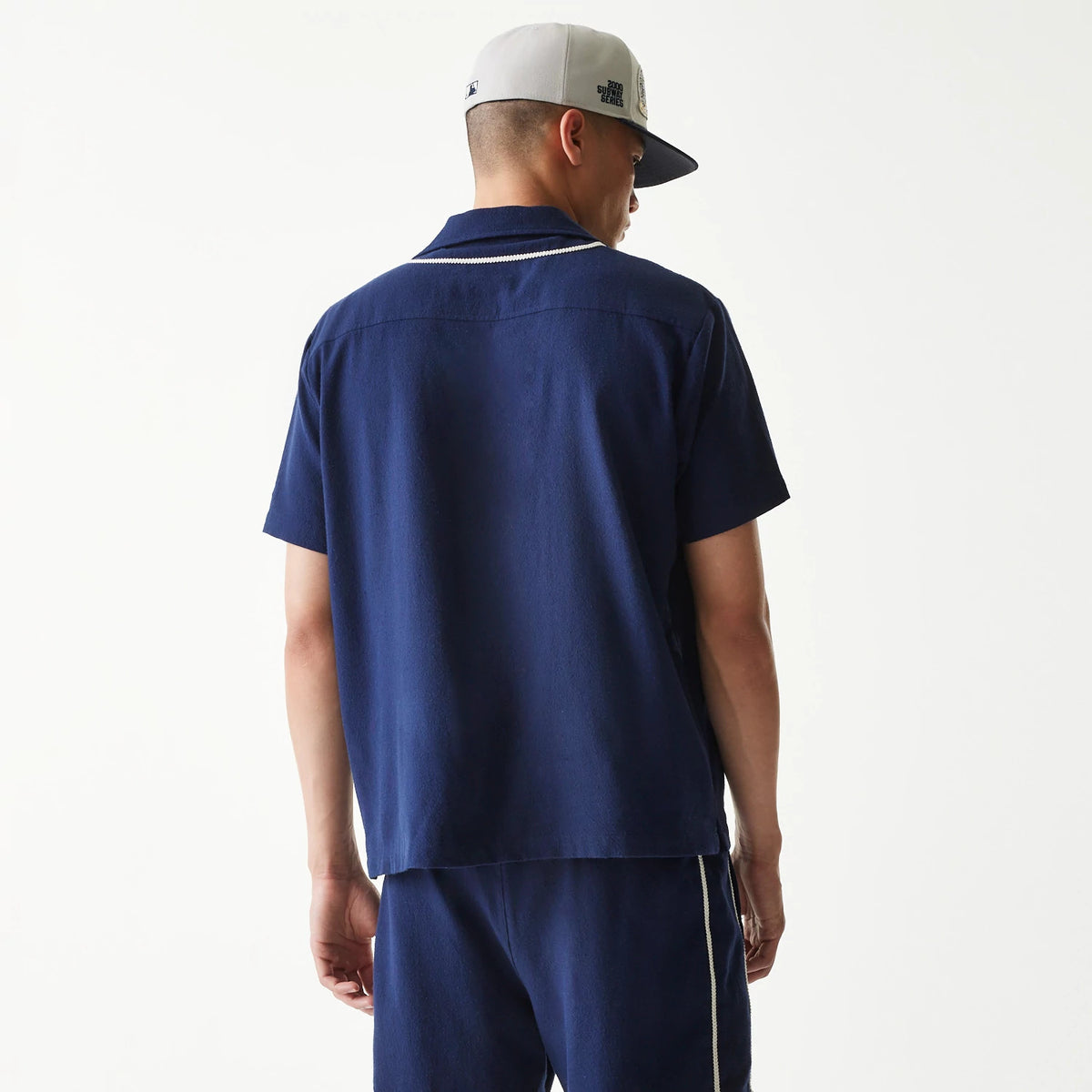 New Era New York Yankees MLB Piping Navy Short Sleeve Shirt, back view on a model with a grey cap, showing the navy shirt with white piping detail along the collar, matching navy shorts, and the structured collar design.
