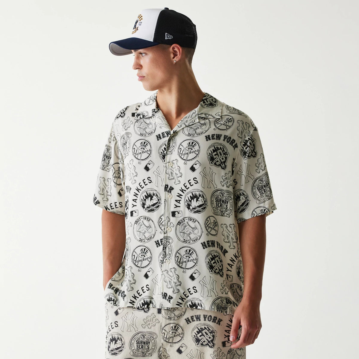 New Era MLB Subway Series All Over Print Open White Short Sleeve Shirt, on-model view showing the intricate black graphic patterns of various MLB team logos, with a relaxed fit and button-up front.