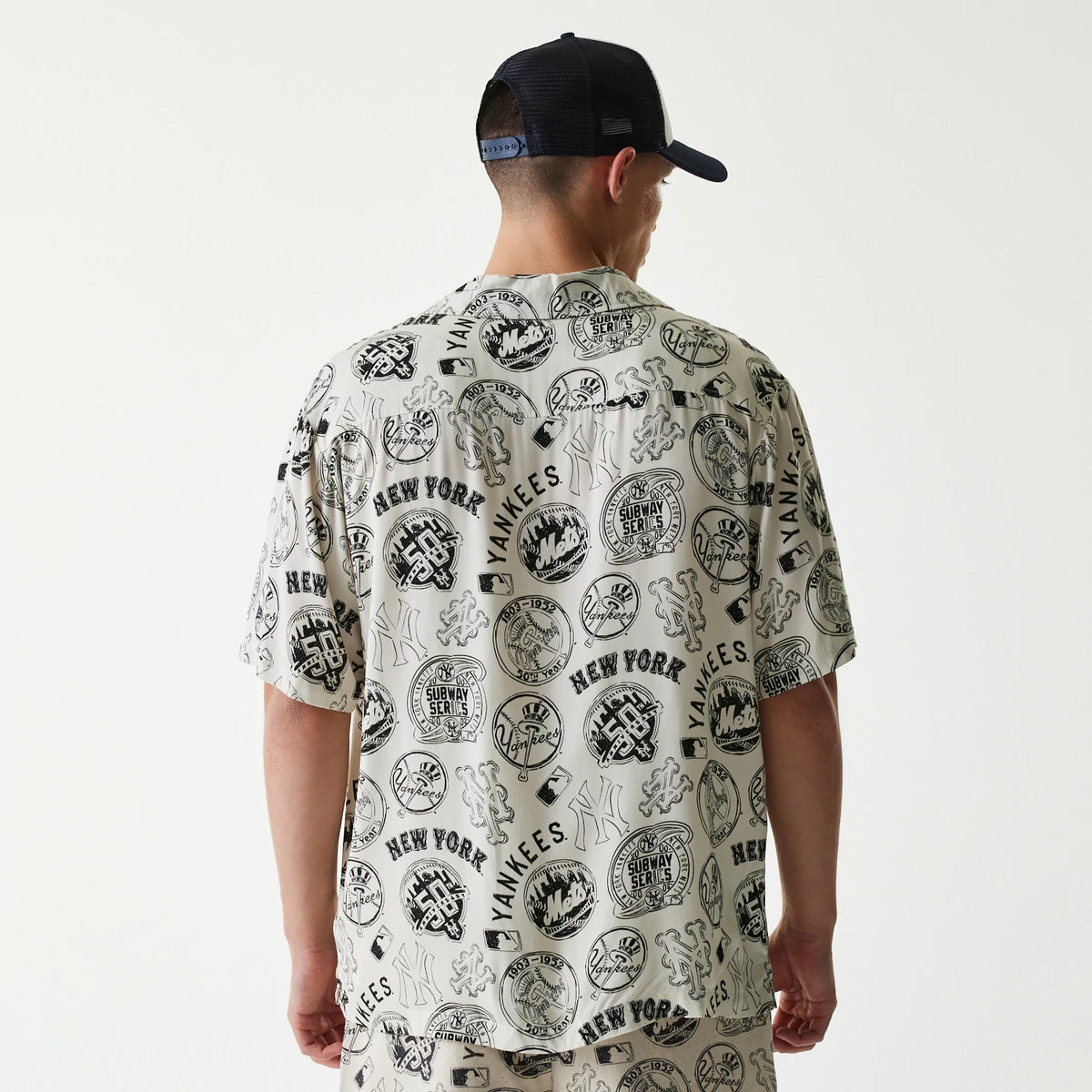New Era MLB Subway Series All Over Print Open White Short Sleeve Shirt, back view on a model wearing a dark cap, showing an intricate collage of Yankees and Mets logos and Subway Series motifs in black across the white fabric.