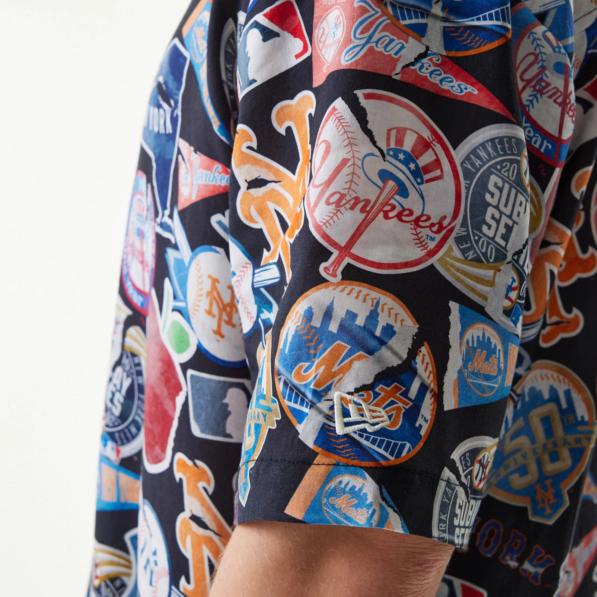 New Era MLB Subway Series All Over Print Navy Short Sleeve Shirt, side view showing a pattern of baseball logos in red, orange, blue and white, with different team emblems, and a small embroidered New Era flag logo above the sleeve hem.