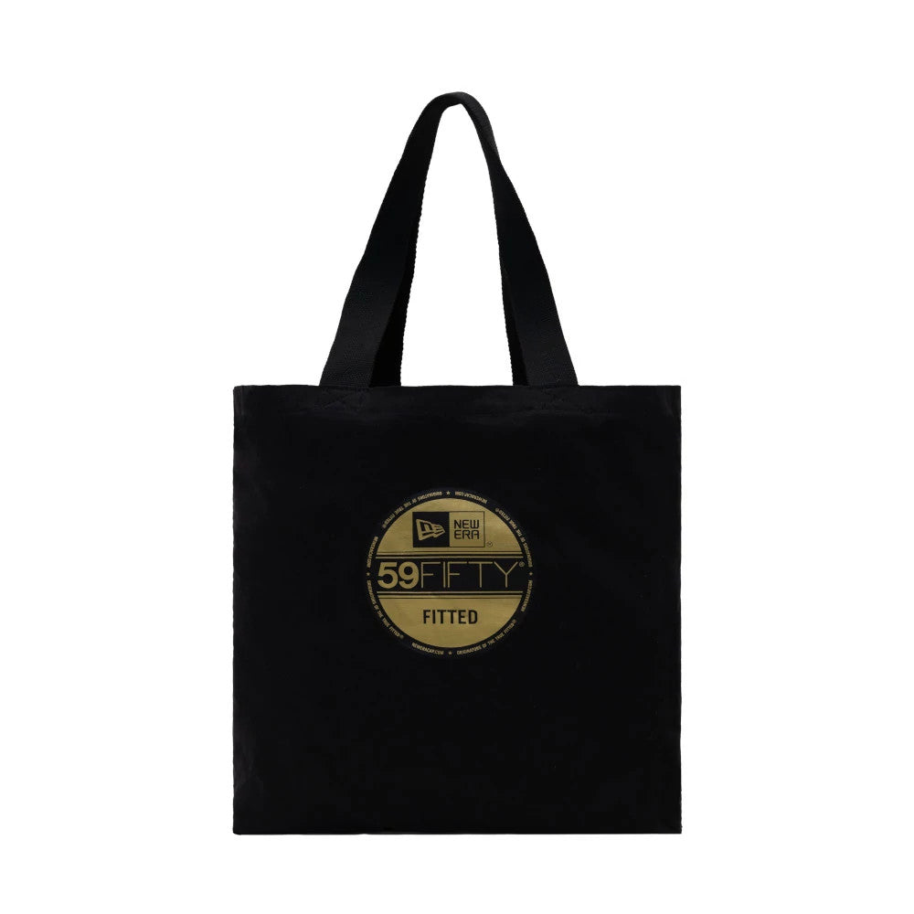 New Era Black Tote Bag, front view showing a large gold printed circular emblem centred on the black tote, featuring the New Era logo and 59FIFTY fitted text, with black handles extending from the top.