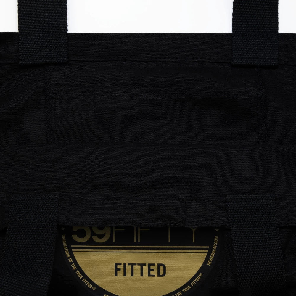 New Era Black Tote Bag, inside view showing the spacious interior with parallel black straps, a hidden pocket along the upper section, and a partially gold 59FIFTY fitted sticker on a cap placed inside.