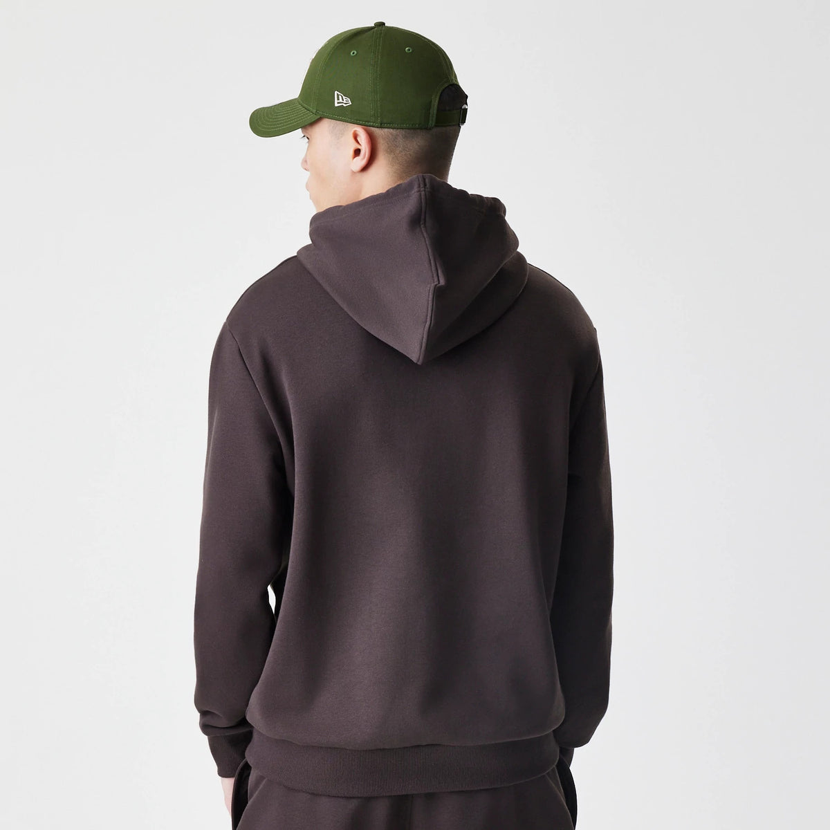 New Era New York Yankees MLB Midi League Essential Dark Brown Oversized Pullover Hoodie, back view on a model wearing a green cap, showing the plain dark brown hood and long sleeves with ribbed cuffs.