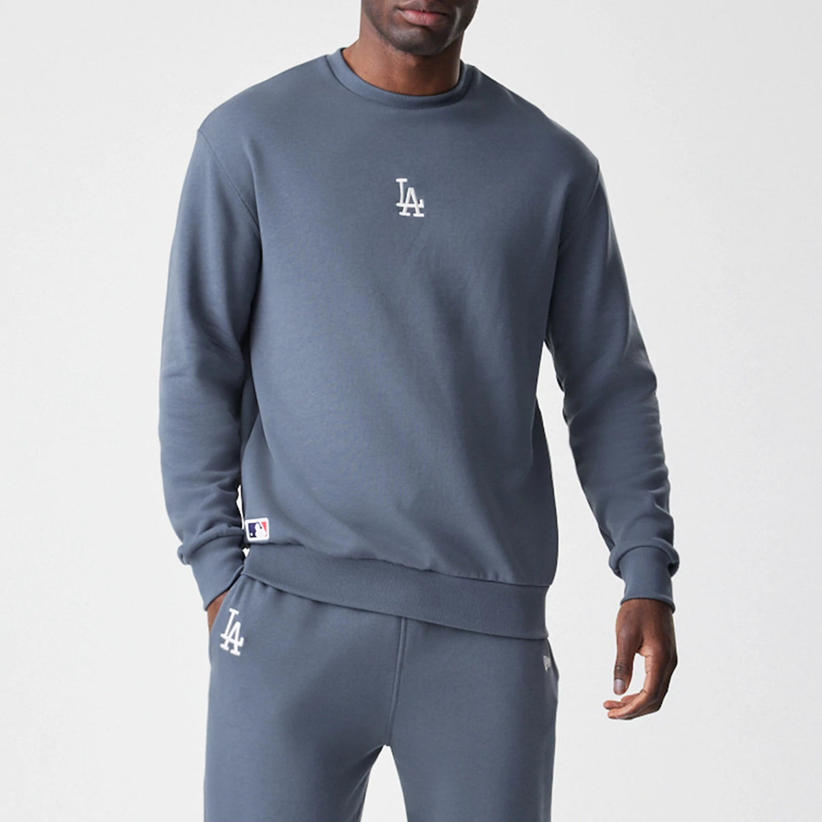 New Era LA Dodgers MLB Midi League Essential Dark Grey Oversized Crew Neck Sweater, front view on a model showing the white LA logo on the chest and the MLB logo on the lower left side above the ribbed hem.
