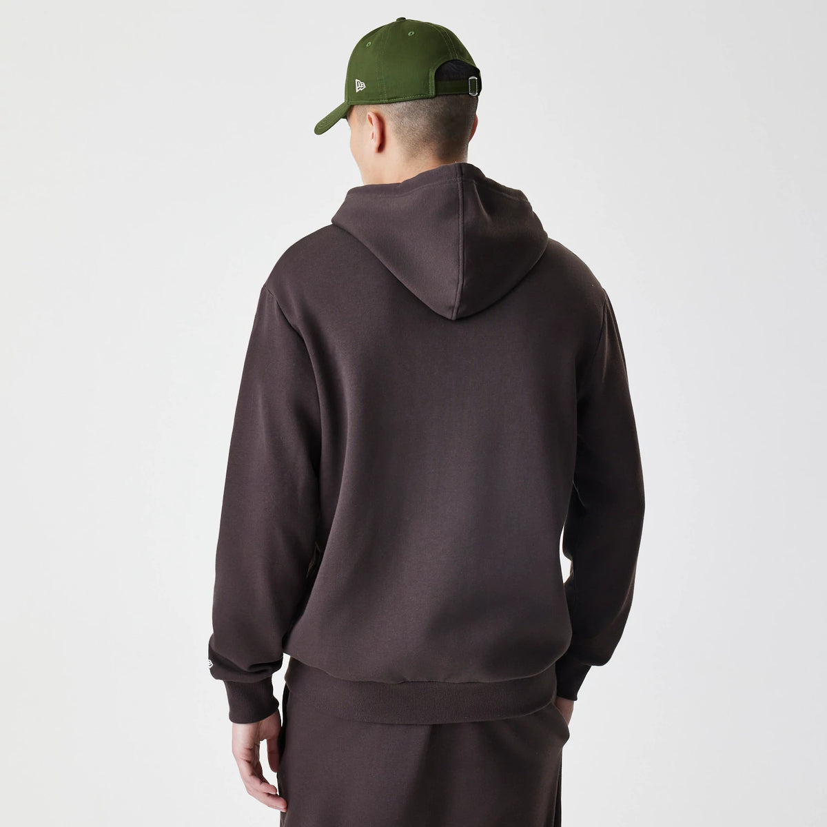 New Era New York Yankees MLB Midi League Essential Dark Brown Full Zip Hoodie, back view on a model wearing a green cap, showcasing the dark brown fabric with a relaxed hood and ribbed cuffs and waistband.