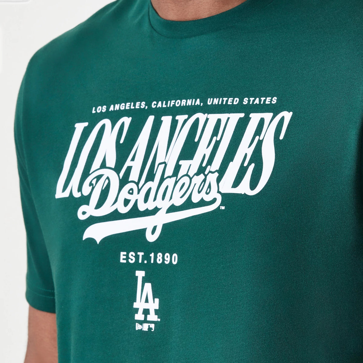 New Era LA Dodgers MLB Script Graphic Dark Green T-Shirt, front view displaying large white lettering of Los Angeles Dodgers across the chest, with Est. 1890 below and an embroidered LA logo at the bottom.