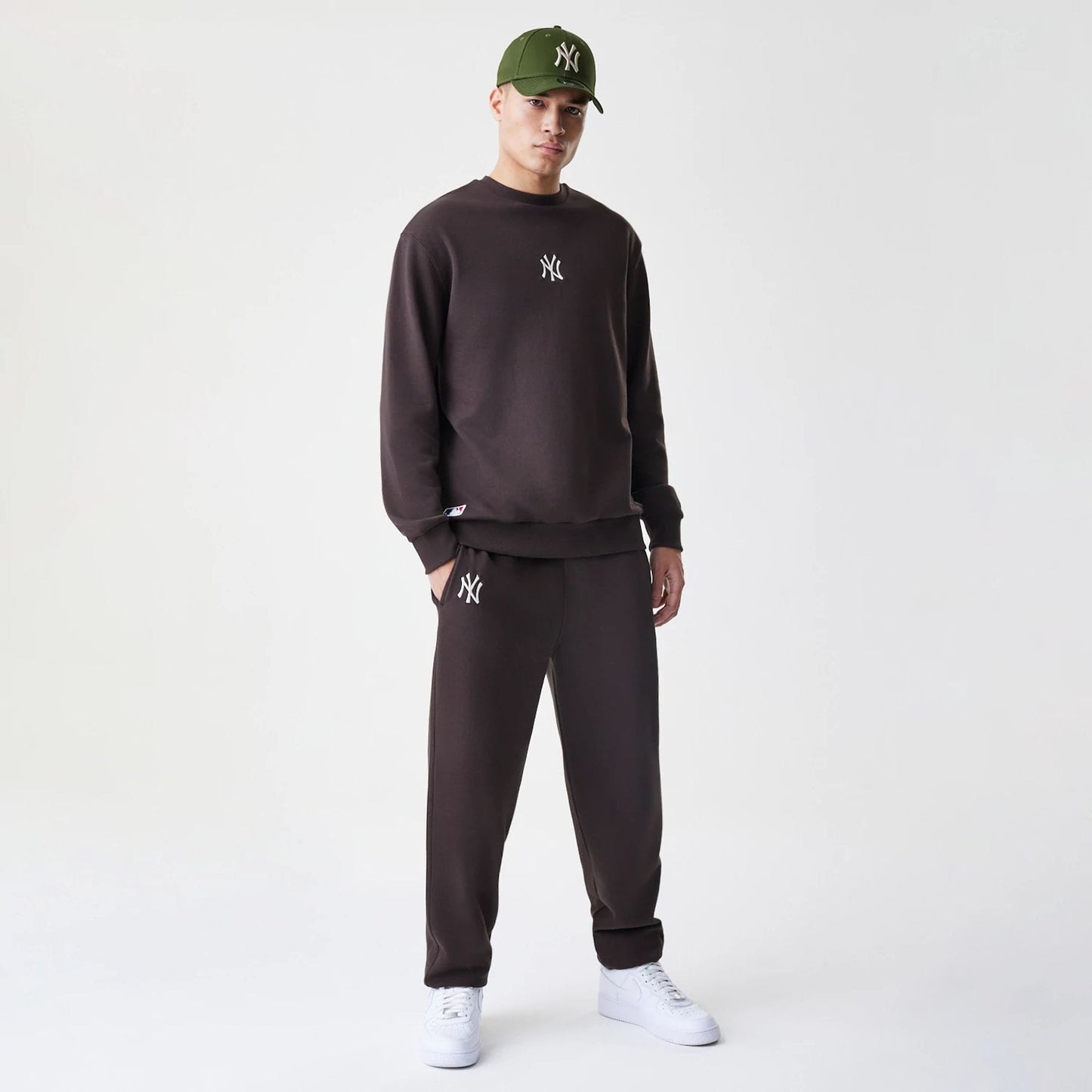 New Era New York Yankees MLB Midi League Essential Dark Brown Oversized Crew Neck Sweater, on-model front view with the NY logo in white embroidery on the chest, paired with matching dark brown trousers and white trainers.