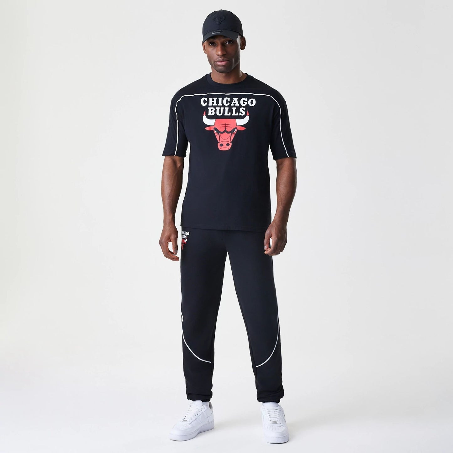 New Era Chicago Bulls NBA Piping Stripe Black Oversized T-Shirt, front view on-model showing the red Bulls logo and white Chicago Bulls lettering across the chest, set against a black background with white piping along the shoulders.